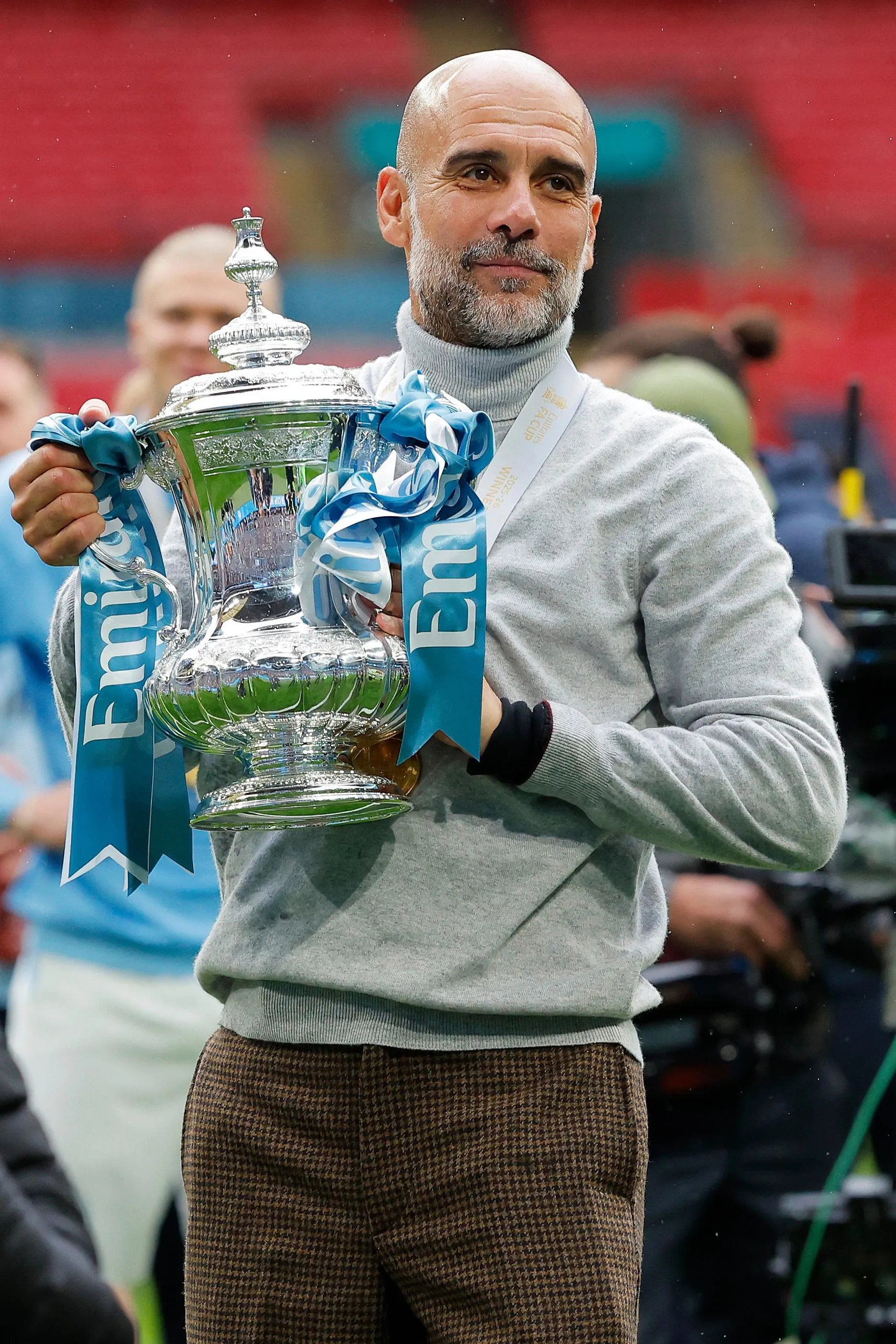 Manchester City manager Pep Guardiola proudly holds the FA Cup trophy.