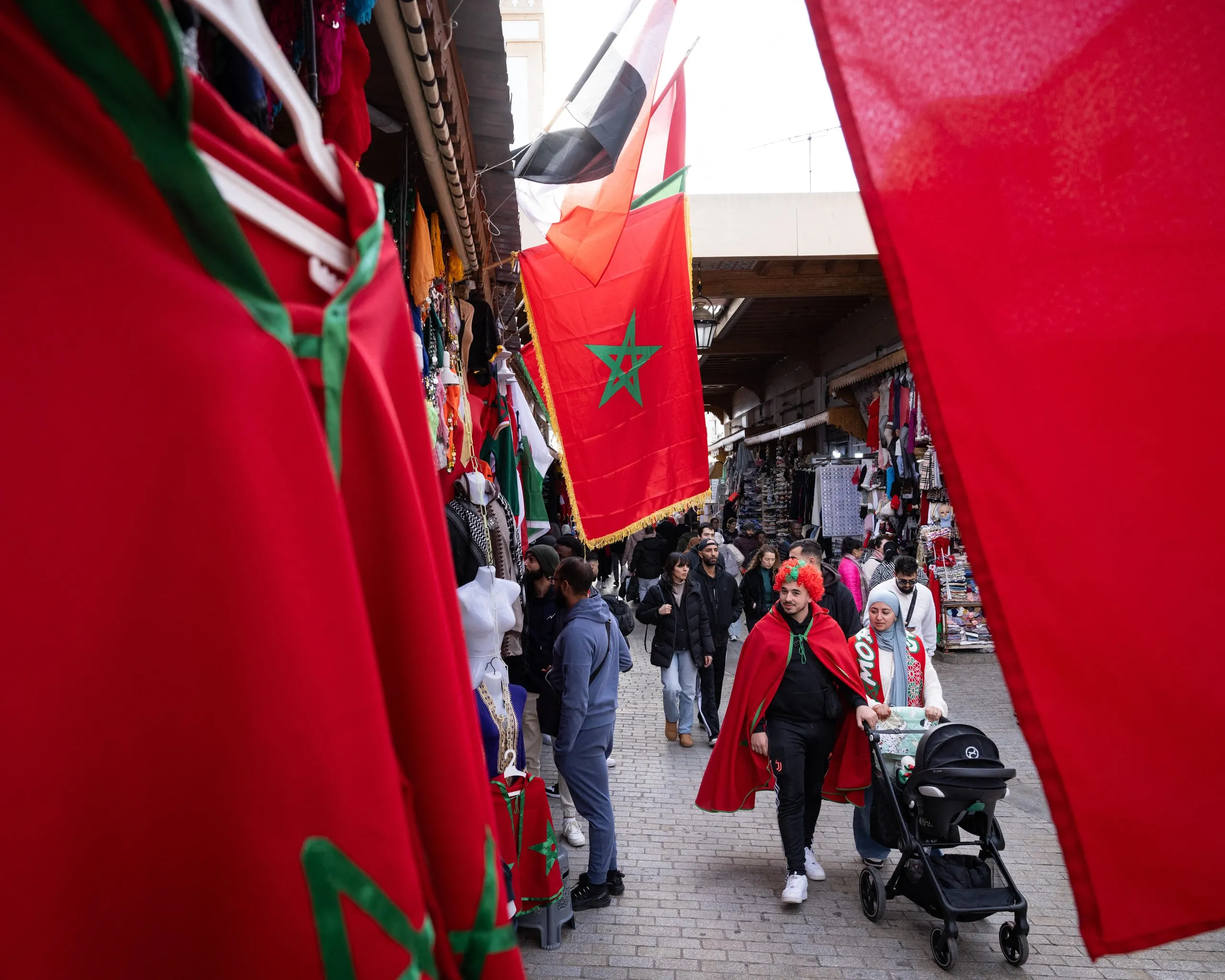 Large flags on the streets, as shoppers walk past in a market 
