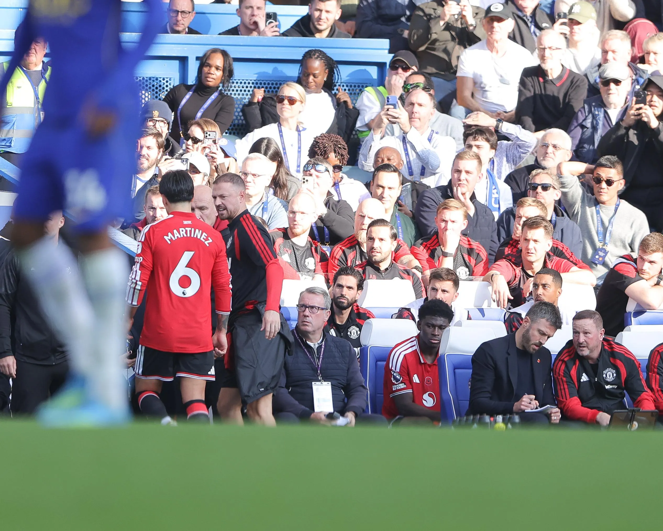 Lisandro Martínez walks down the tunnel after being sent off at Stamford Bridge as Michael Carrick makes notes on the bench.
