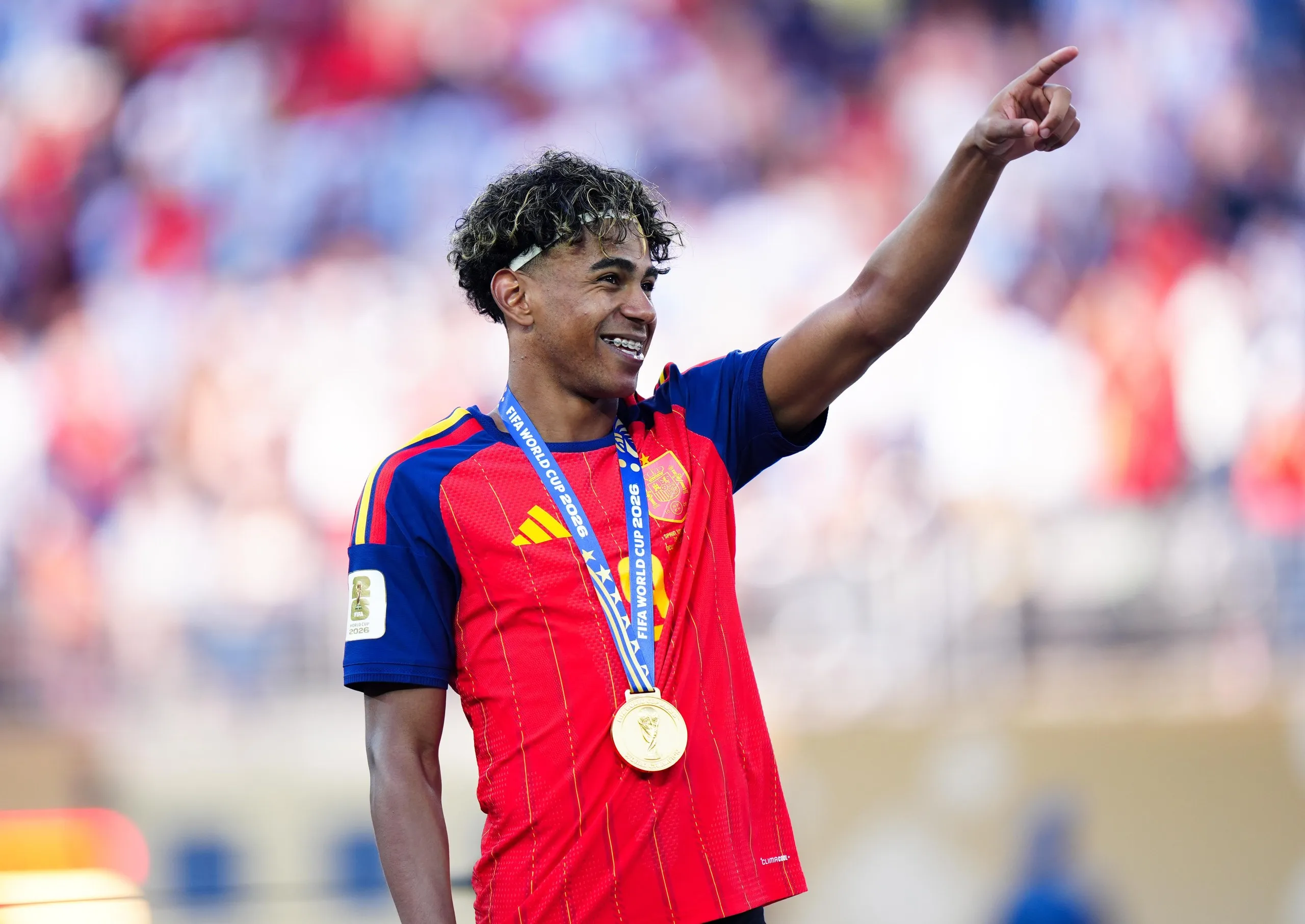 Lamine Yamal, wearing a gold medal, smiles and points upward after the World Cup final